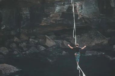 Mann balanciert auf einer Slackline hoch über einer Felsschlucht mit Wasser