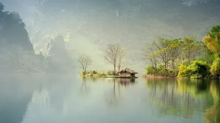 Kleine bewaldete Insel mit Hütte in einem nebligen See