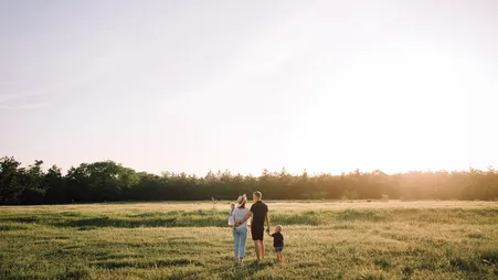 Familie mit Kind geht bei Sonnenuntergang über eine Wiese