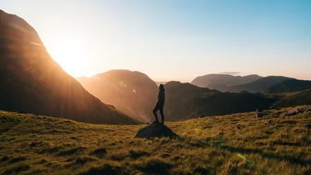 Person steht bei Sonnenaufgang auf einem Felsen in den Bergen