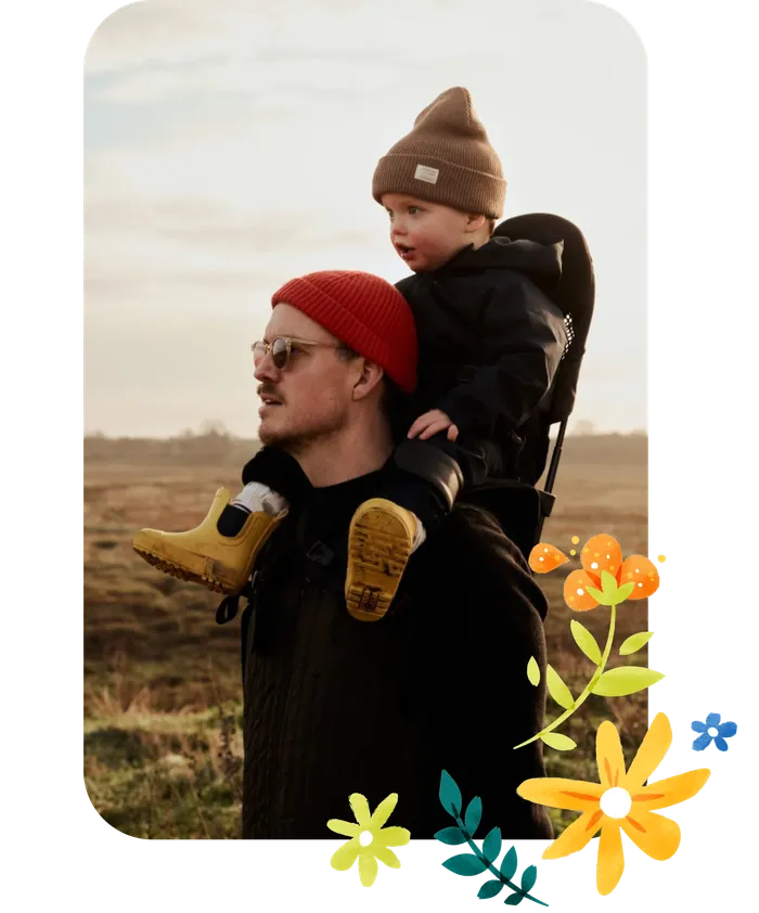 Ein Vater trägt seinen Sohn auf den Schultern durch die Natur.