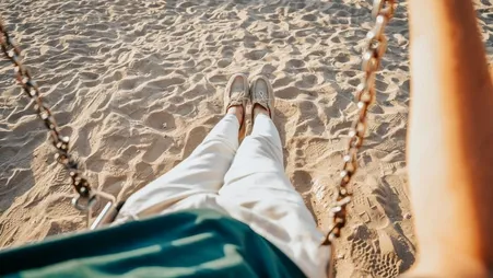 Blick aus einer Strandschaukel auf die eigenen Beine und den Sand